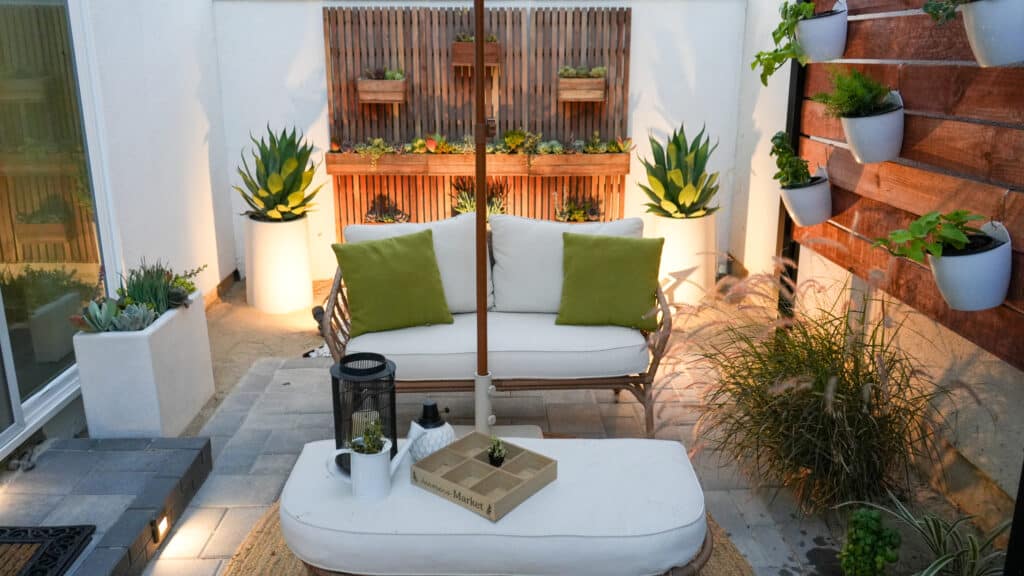 A side yard patio shows  various wall planters and pots with succulents and green plants. Shown is a white patio furniture set.