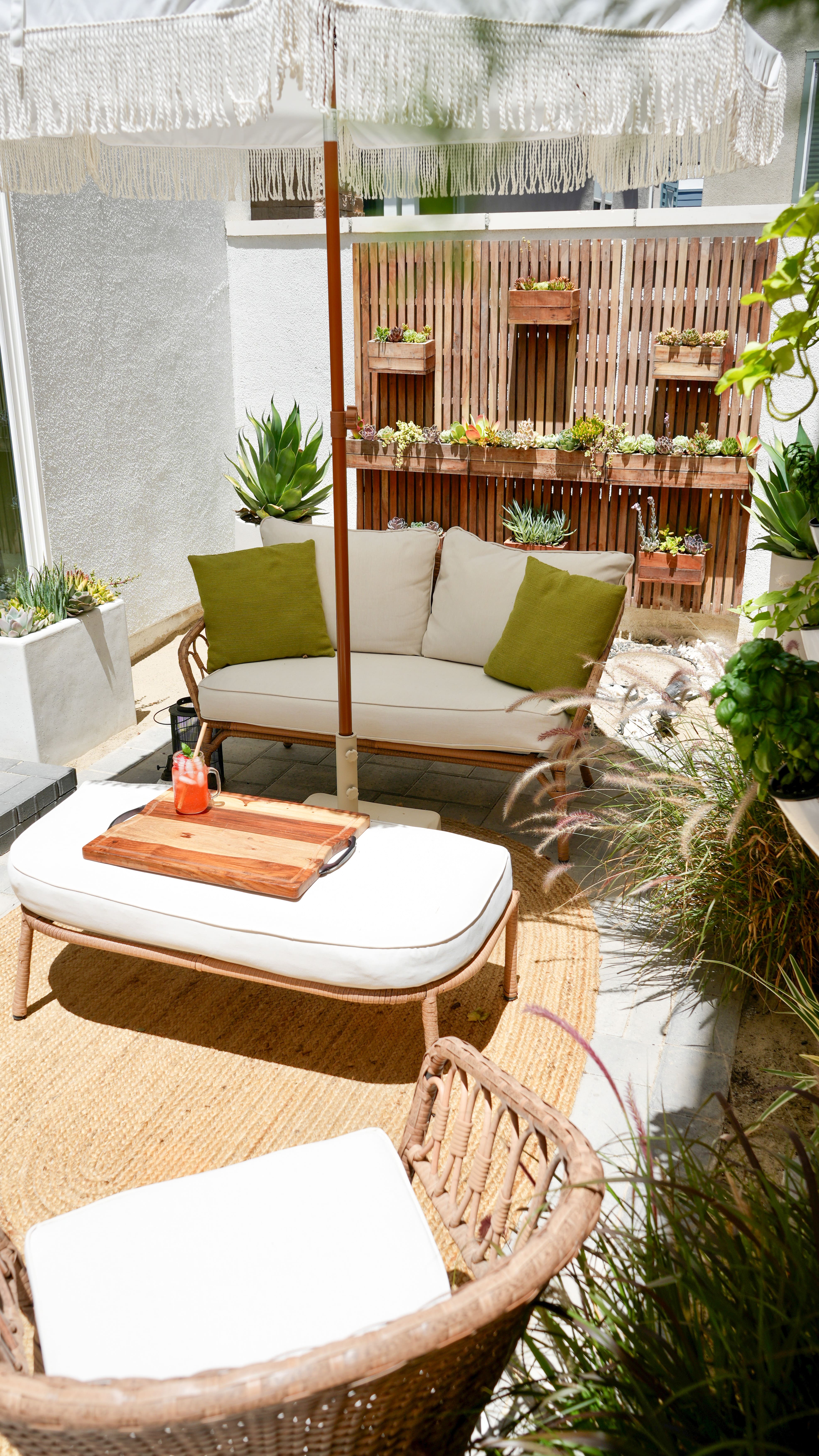 Side yard patio featuring wall planters with green plants, white patio furniture with green pillows and a white patio umbrella.