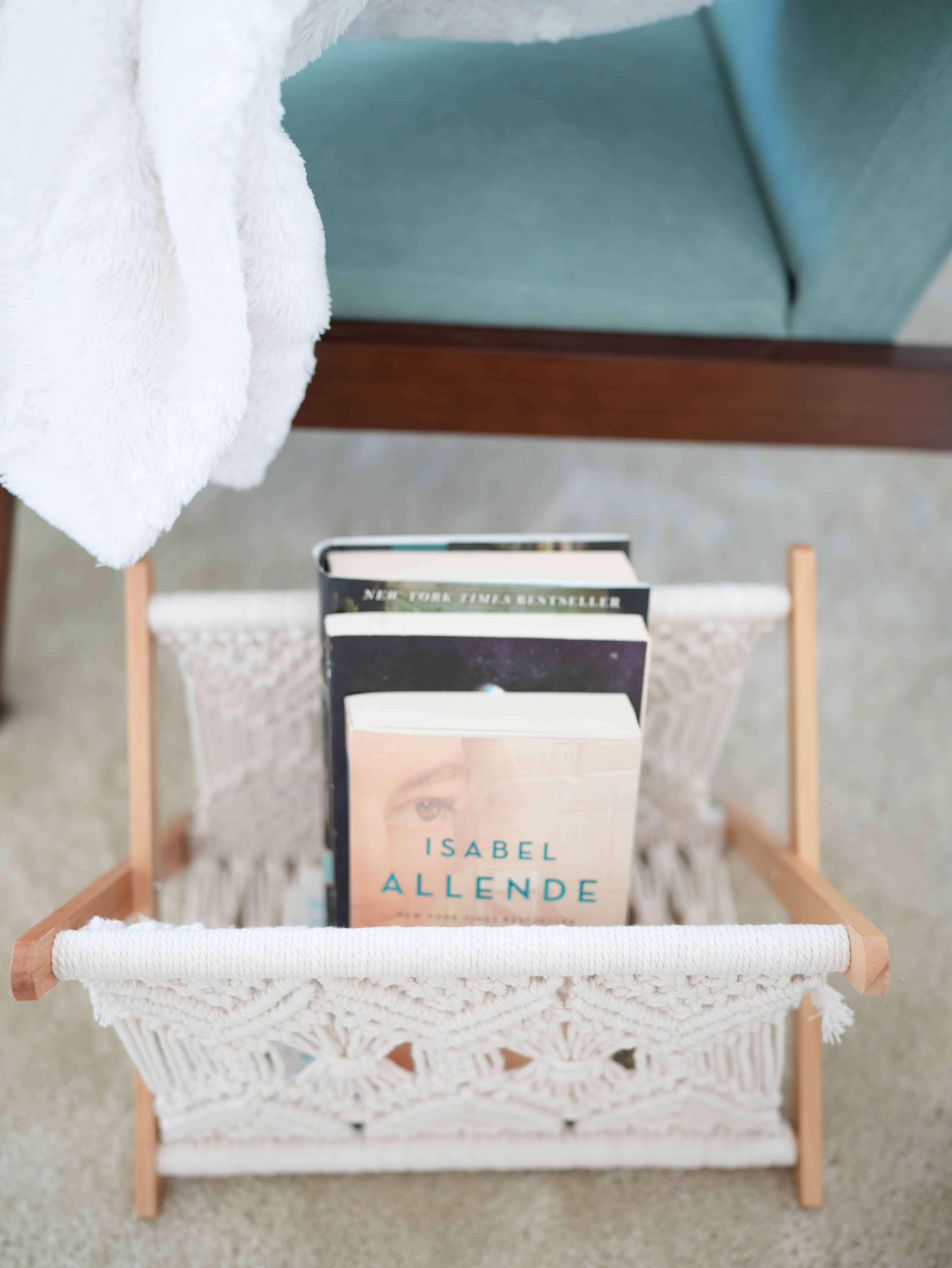 Magazine holder made of wood and crocheted yarn. Holding three books, one with a cover that reads "Isabel Allende".