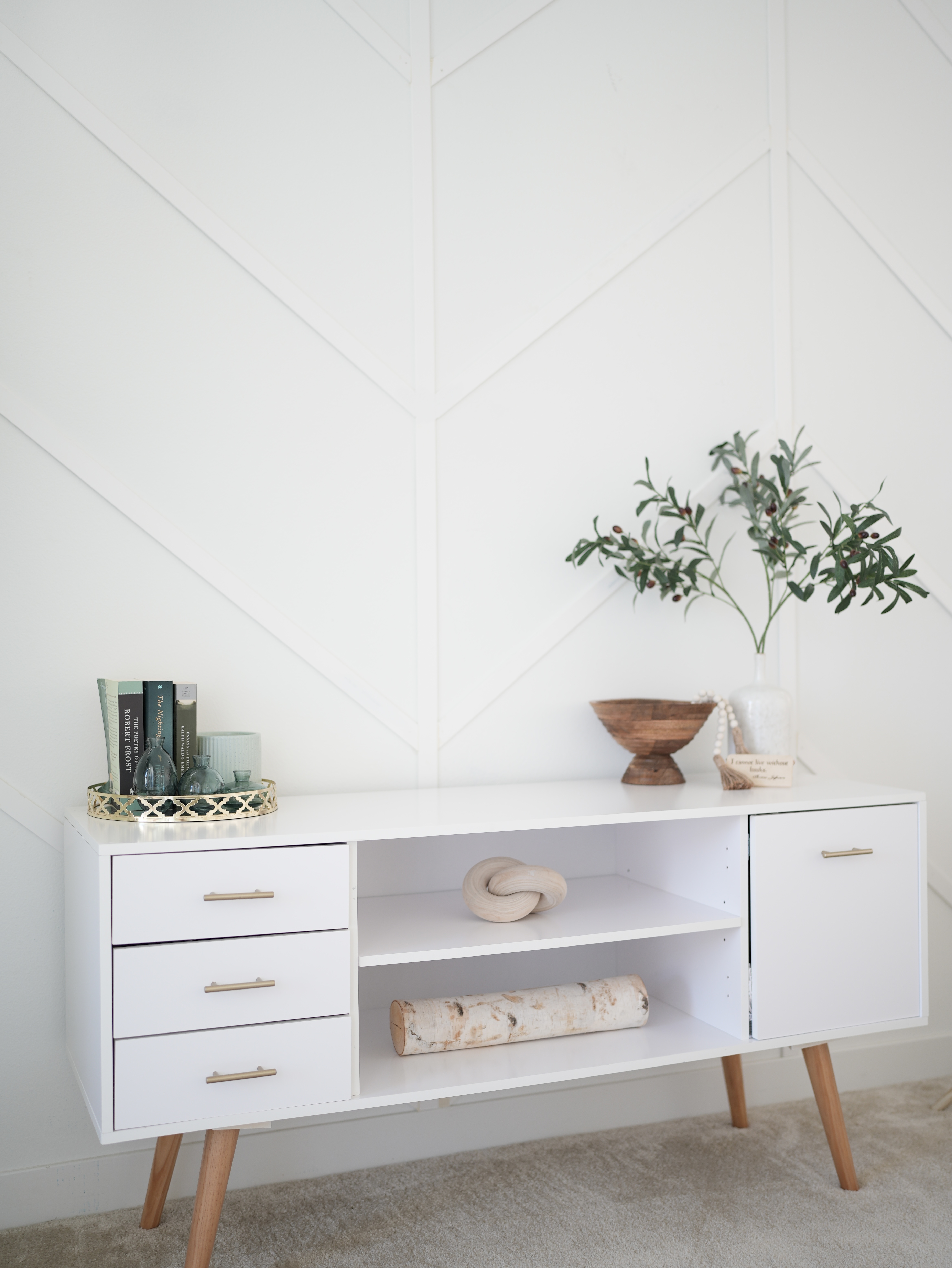 Long white console table with wooden legs, against a white accent wall. 