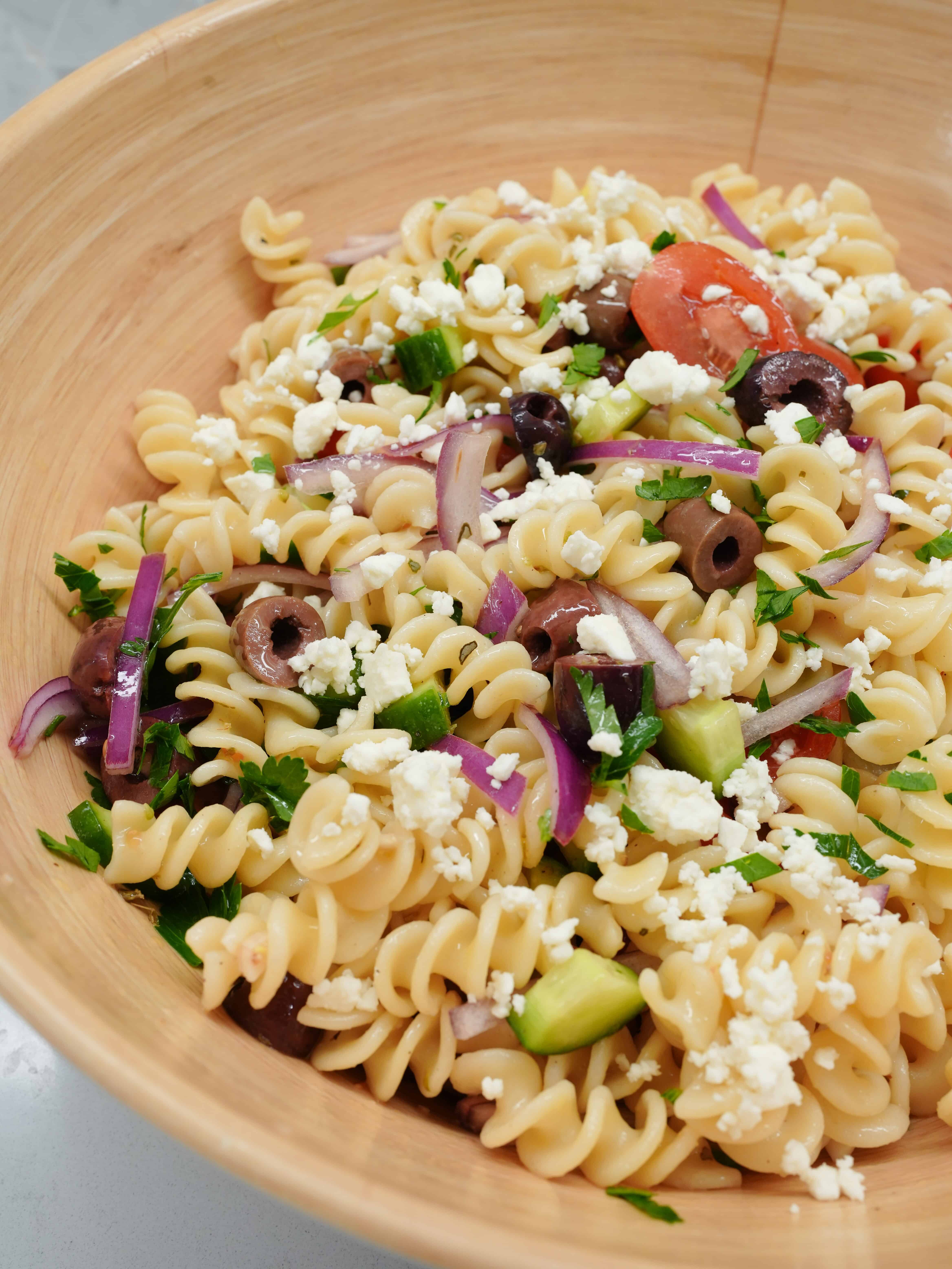 Greek Pasta Salad with rotini pasta, red onions, tomatoes, olive, and feta cheese served in a large pasta bowl