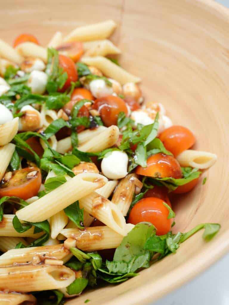 Caprese Pasta Salad with penne pasta, mozerella pearls, balsamic glaze, basil, and cherry tomatoes.