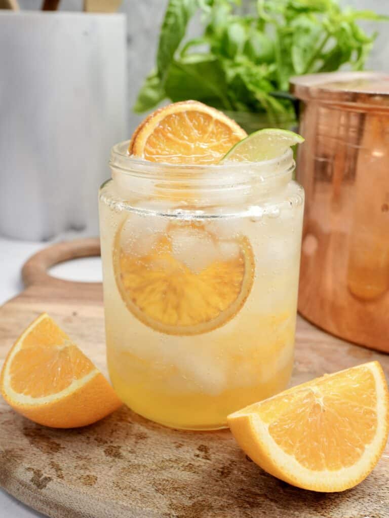 Candied dried oranges in glass jar with sparkling water. Placed on wooden cutting board in front of copper pot and basil plant
