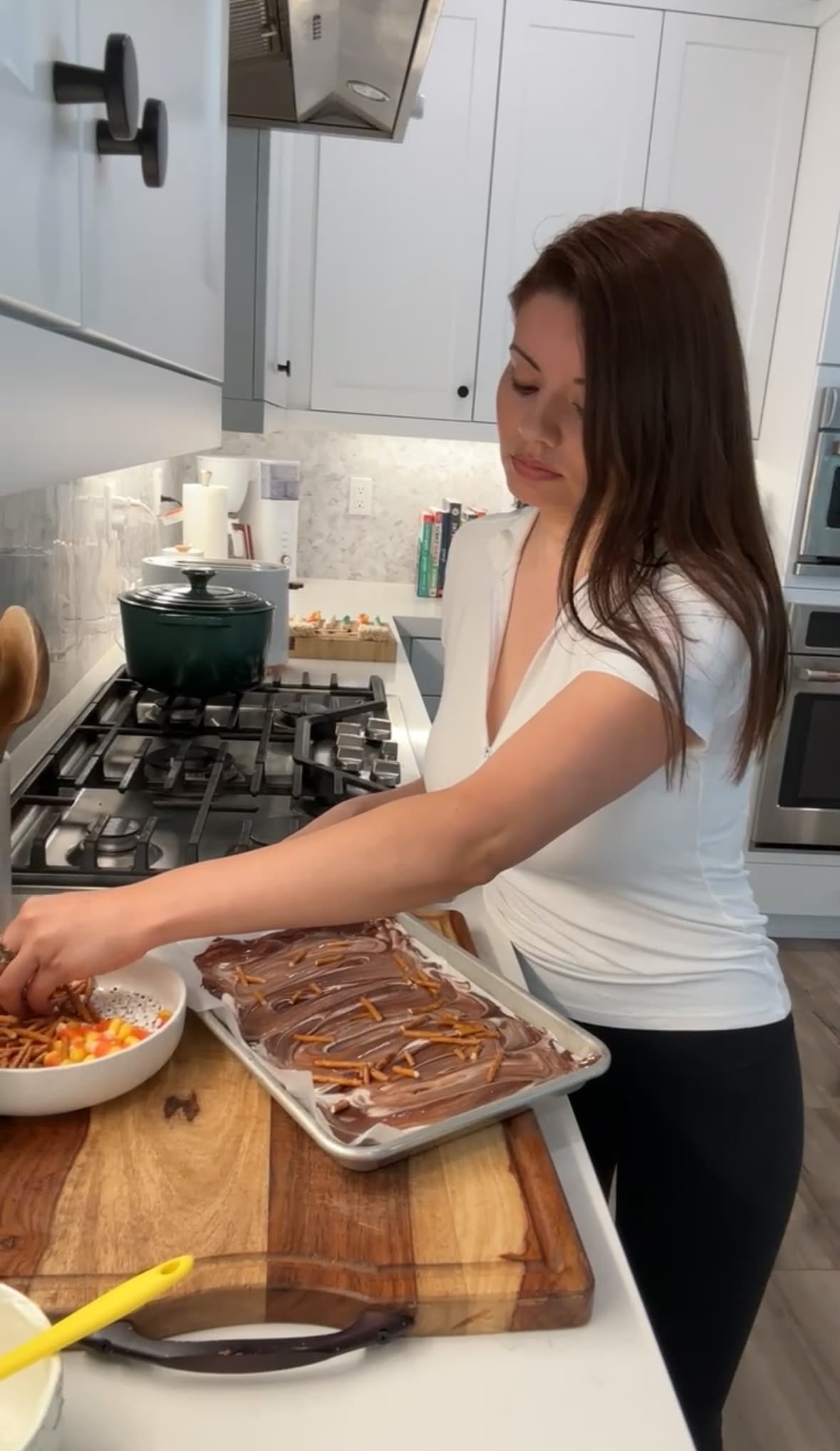 Woman topping chocolate bark with topping including candy corn and pretzels