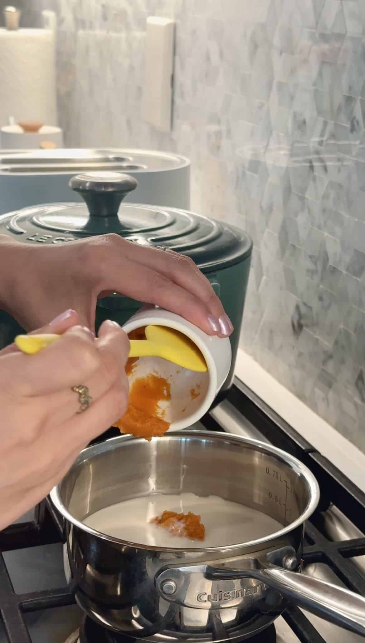 Pumpkin puree going into small pot on the stove filled with milk