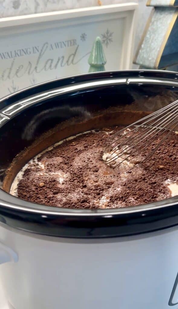 Whisk stirring creamy hot chocolate inside a slow cooker.