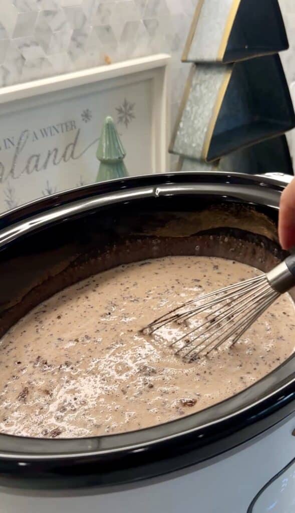 Whisk stirring creamy hot chocolate inside a slow cooker.