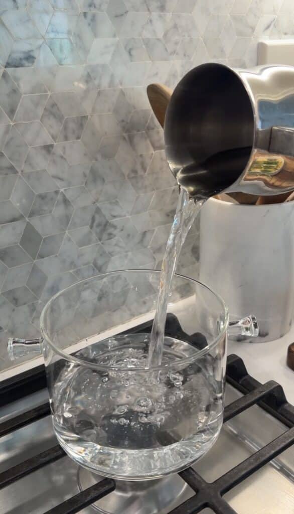 Metal cup pouring water into glass pot on stovetop