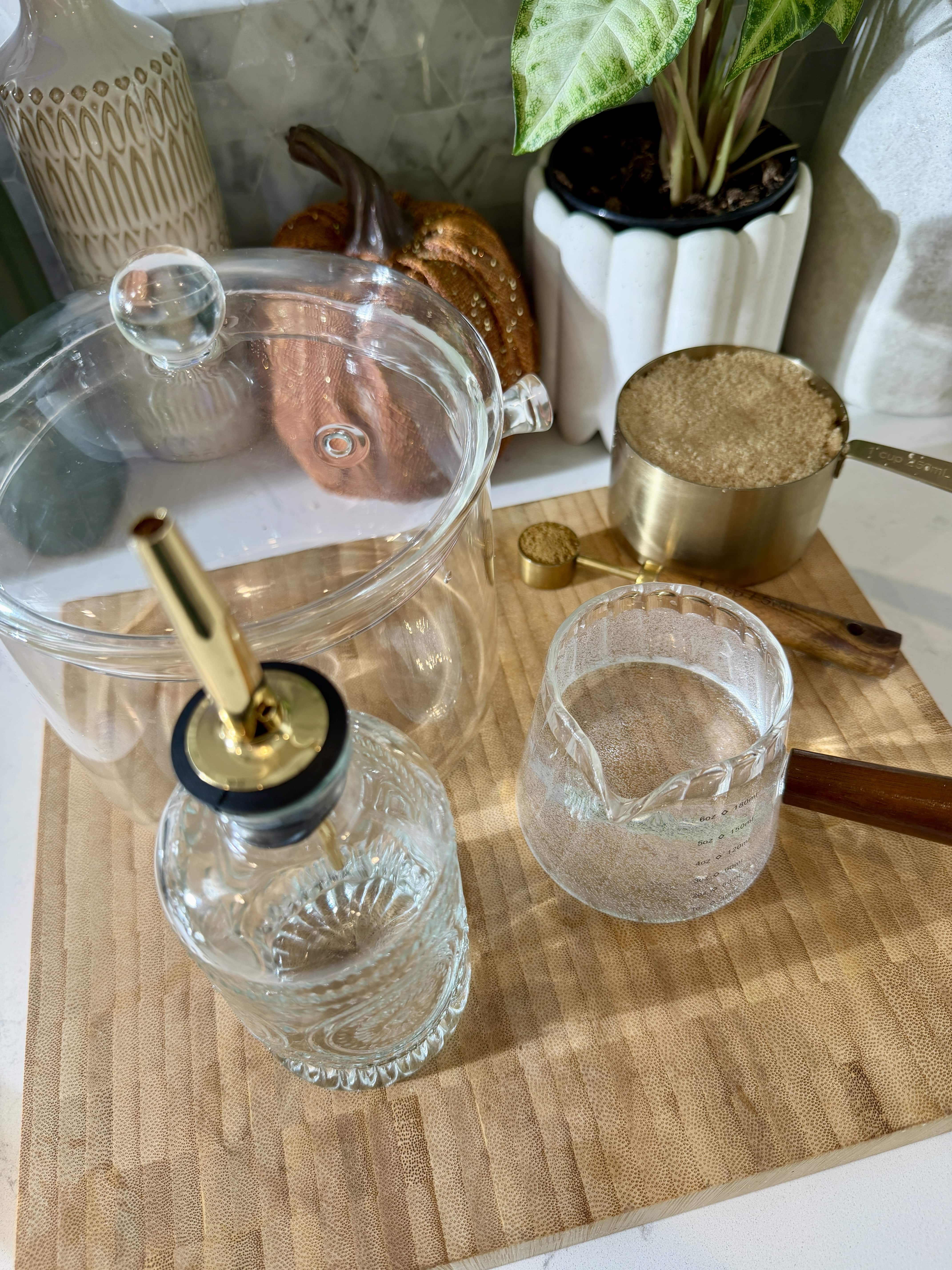 Ingredients and supplies for making brown sugar latte. glass simmer pot, glass syrup dispenser, brown sugar in measuring cup, cup of water